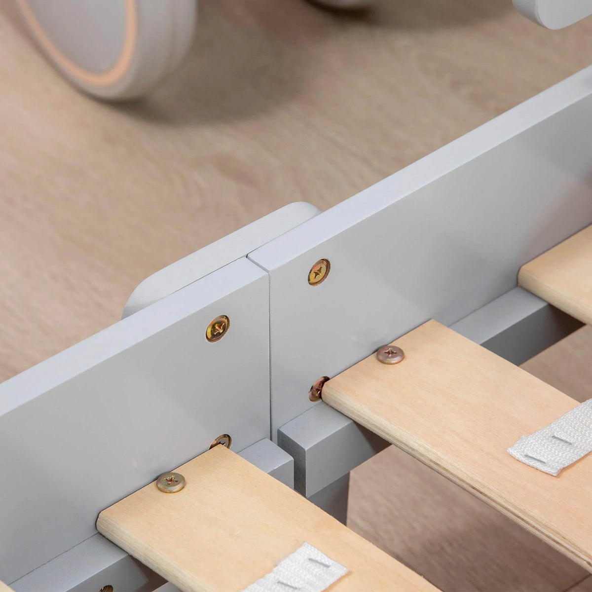 Grey toddler bed frame corner with wooden rails and fasteners