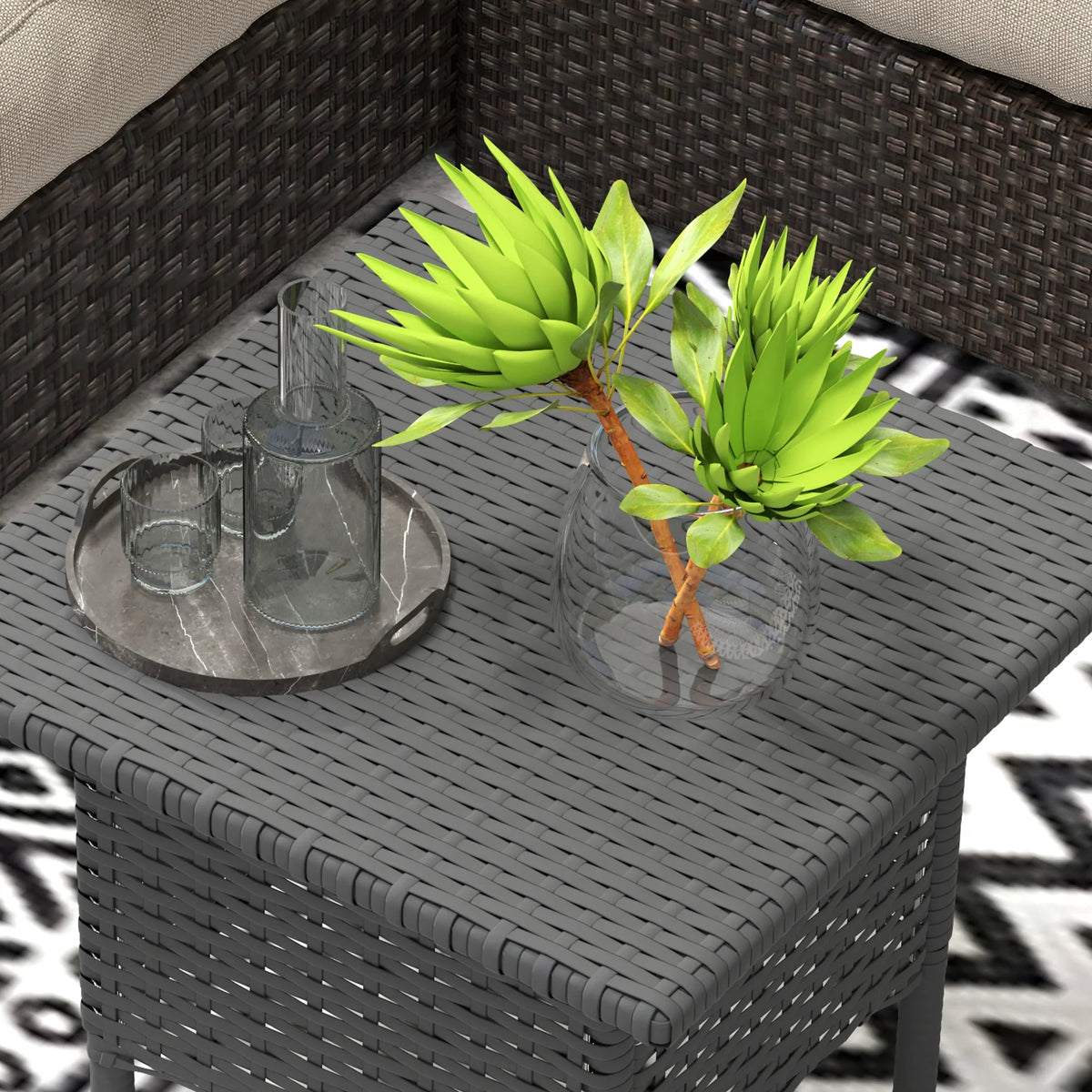 Grey woven outdoor side table with square top, glass cup, and potted plant