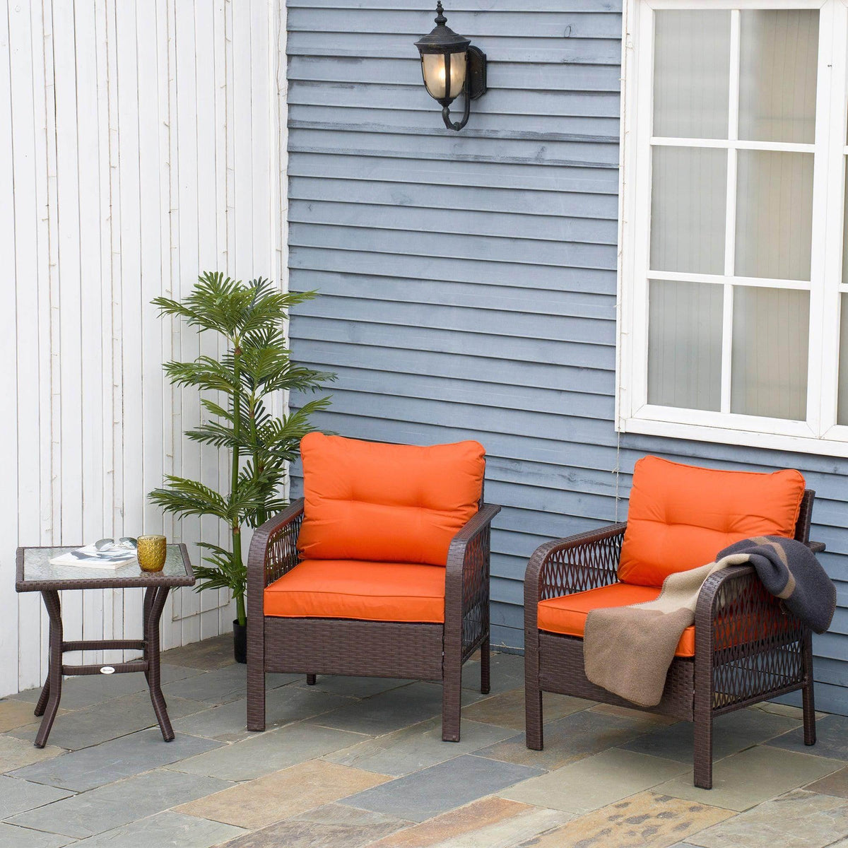 Outdoor wicker bistro set with two orange cushioned chairs and dark brown woven armrests