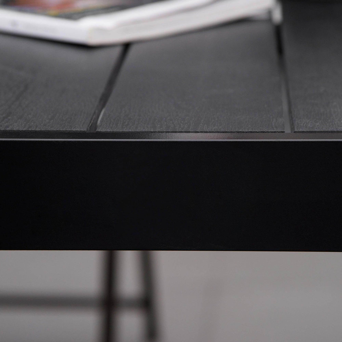 Black table leg and support bracket under faux-wood tabletop, outdoor dining table.