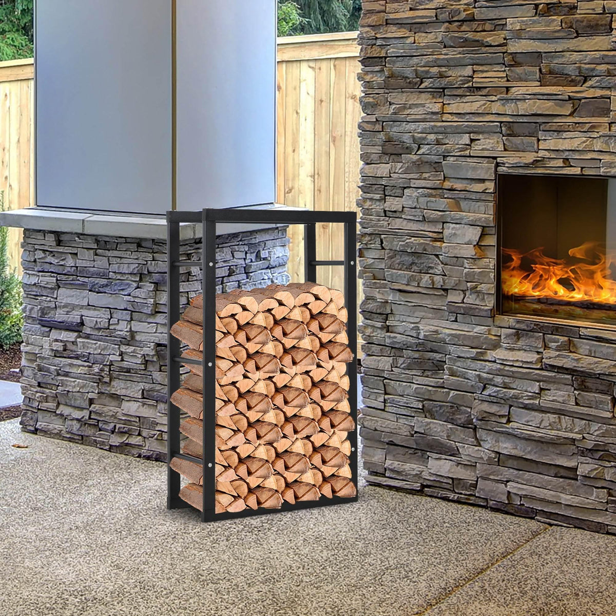 Outdoor tall black metal log holder with stacked firewood next to stone fireplace