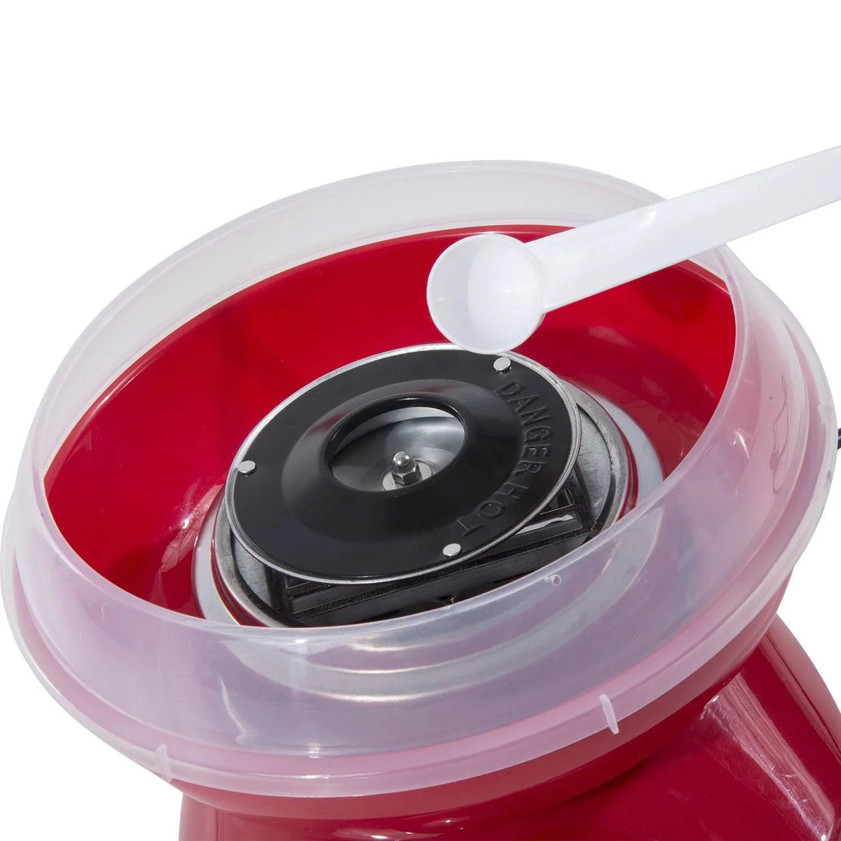 Red cotton candy maker with clear bowl and white measuring spoon over plate