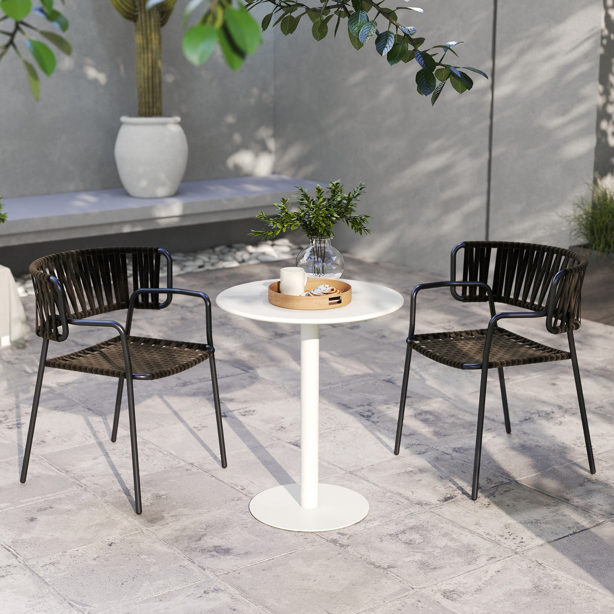 White round patio dining table with pedestal base and two dark metal chairs