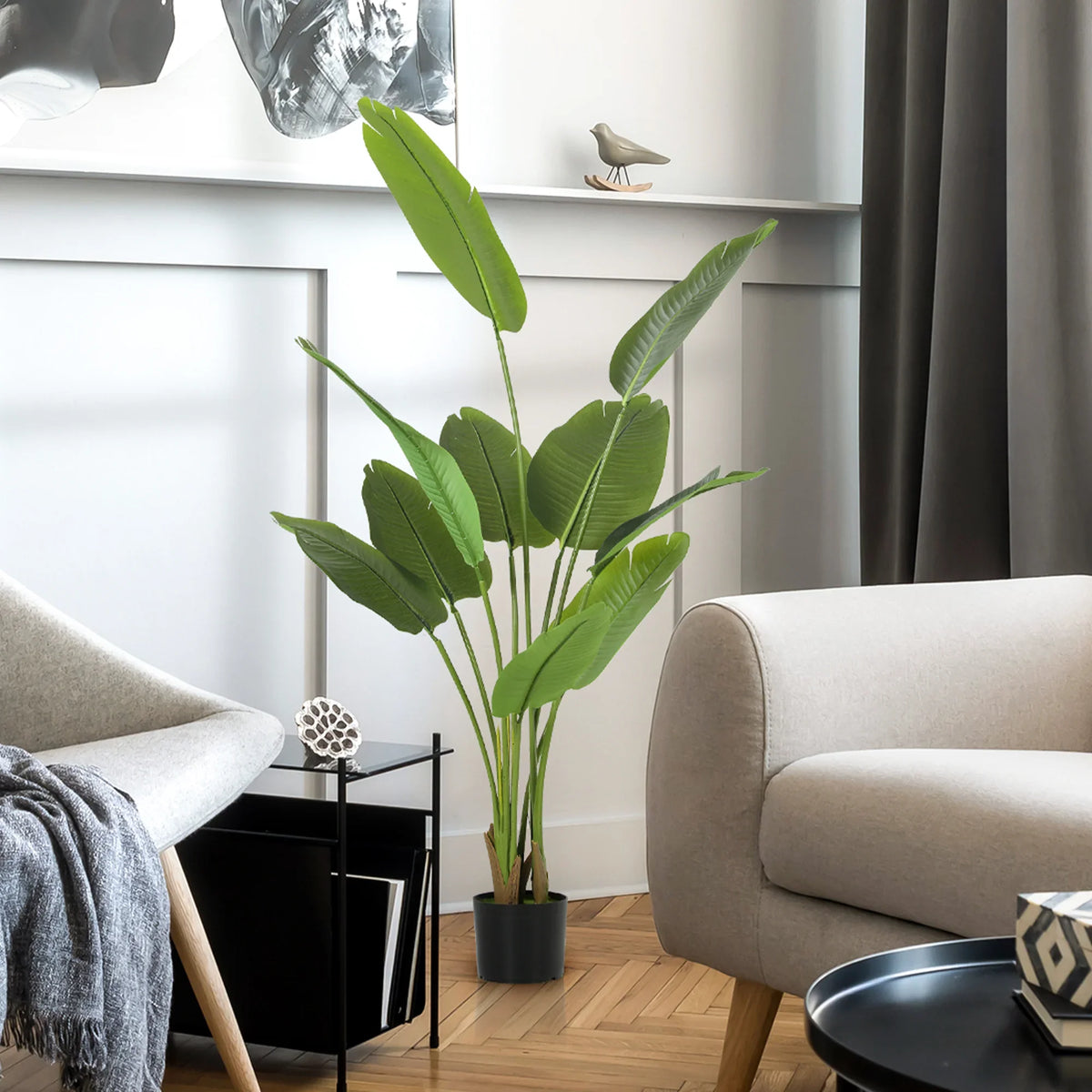 Artificial bird of paradise plant in black pot on floor near beige armchair