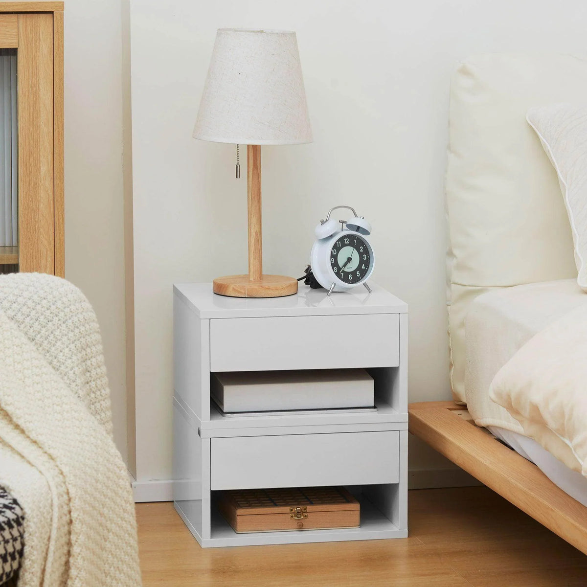 White bedside table with open shelf and drawer beside lamp and sofa seating