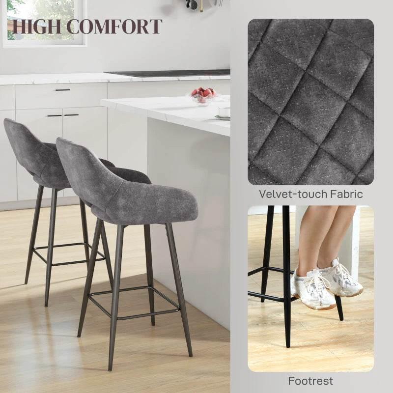 Set of 2 grey velvet bar stools with tufted texture, backrest, and footrest.