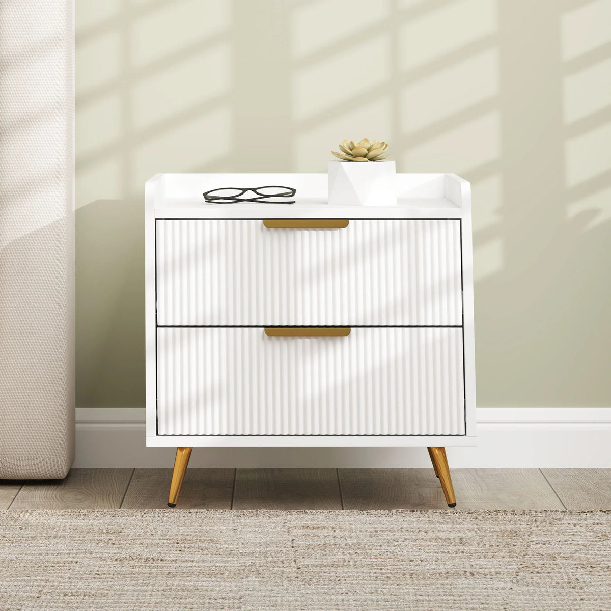 White two-drawer bedside cabinet with ridged drawer panels, gold pulls, and tapered legs
