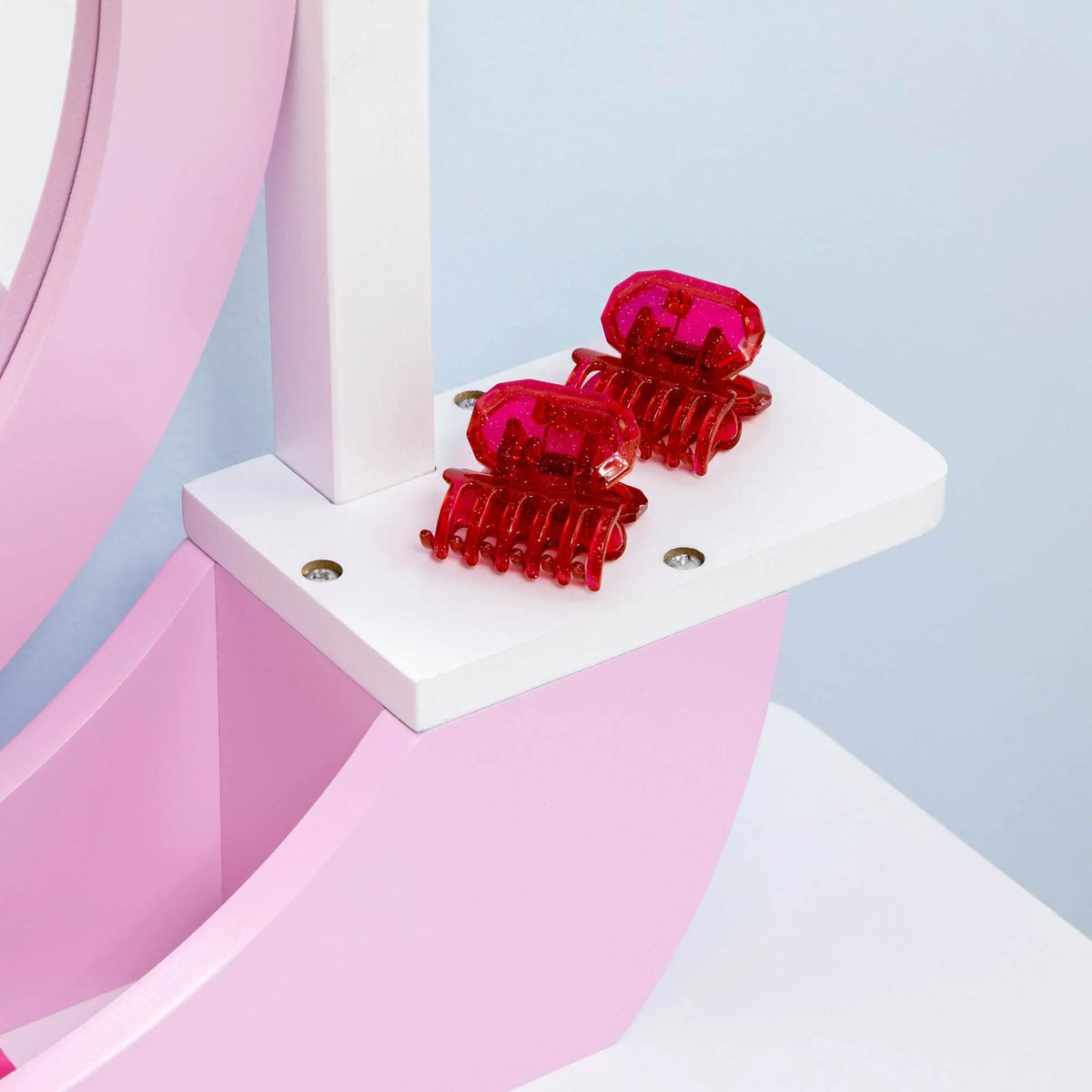 Pink vanity drawer front with two decorative red pull knobs on a white tabletop shelf