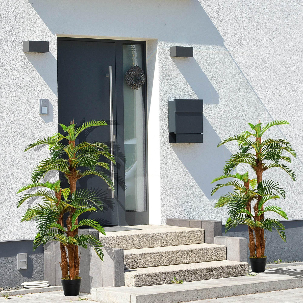 Set of two artificial tropical palm plants in black pots, green fronds, brown trunks