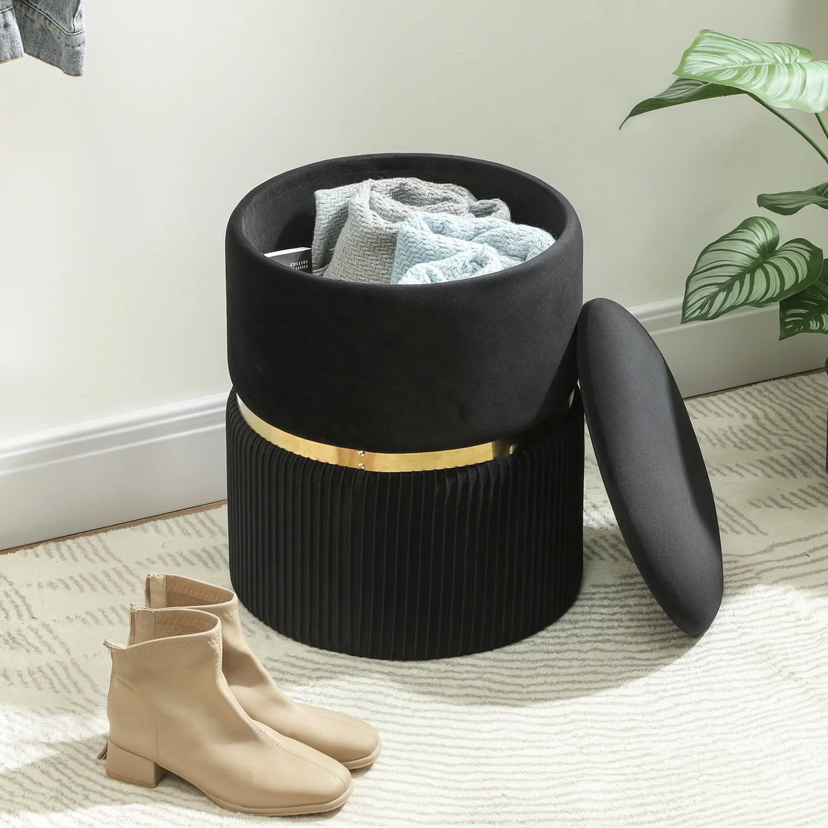 Black storage ottoman with side handle, velvet-look lid, ribbed base, gold-tone band