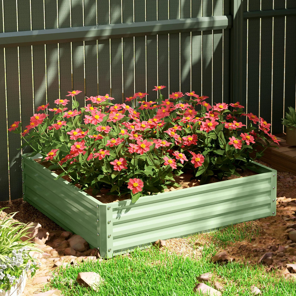 Light green raised planter box with pink flowering plants in outdoor ground