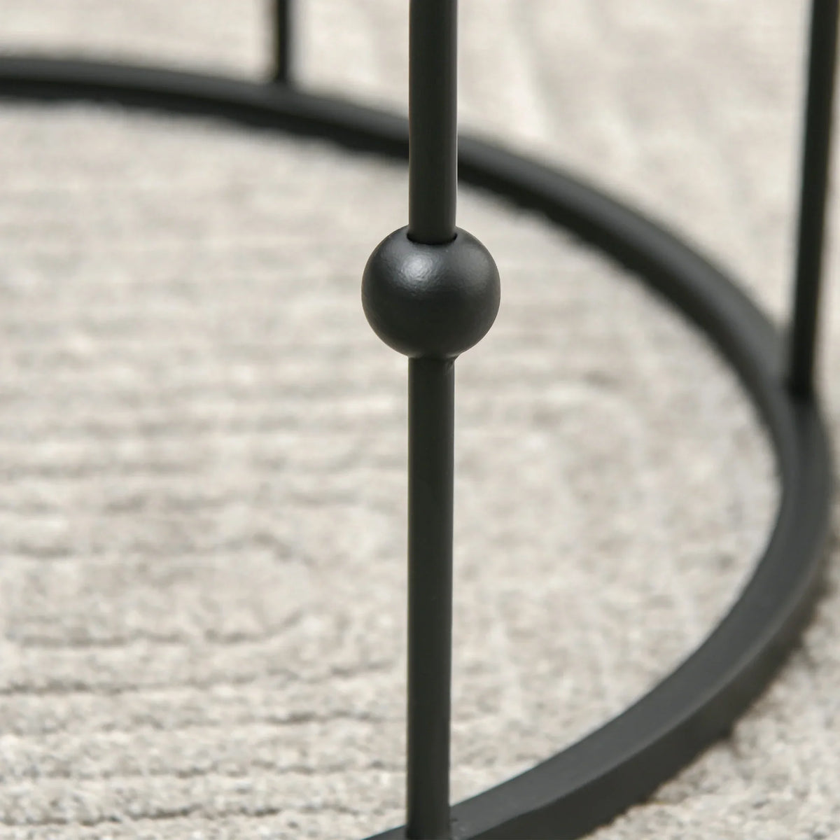 Black metal hoop frame support post on round nesting coffee table with ball end