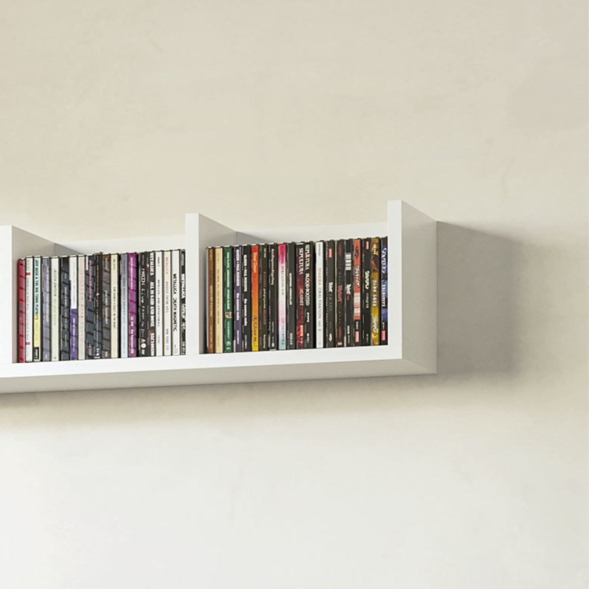 White wall-mounted CD/DVD rack with 4 open cubbies holding stacked cases