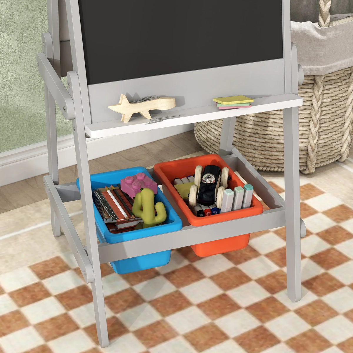 Kids art easel shelf with blue and orange storage bins holding crayons and markers