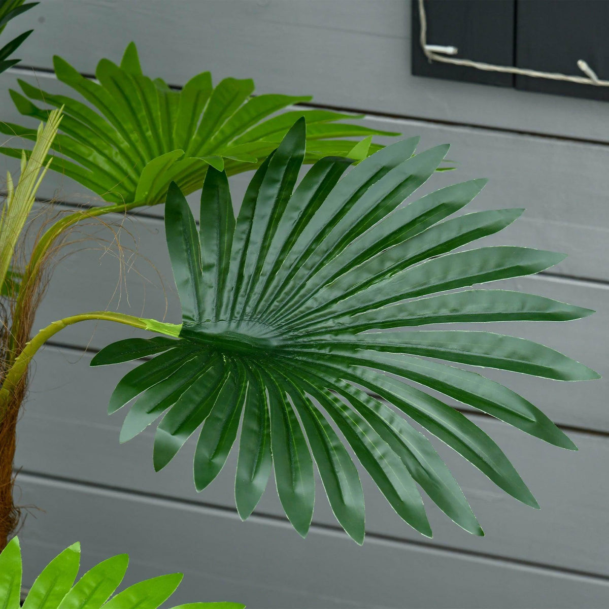 Close-up of artificial palm leaves with layered green fronds and brown trunk in pot.