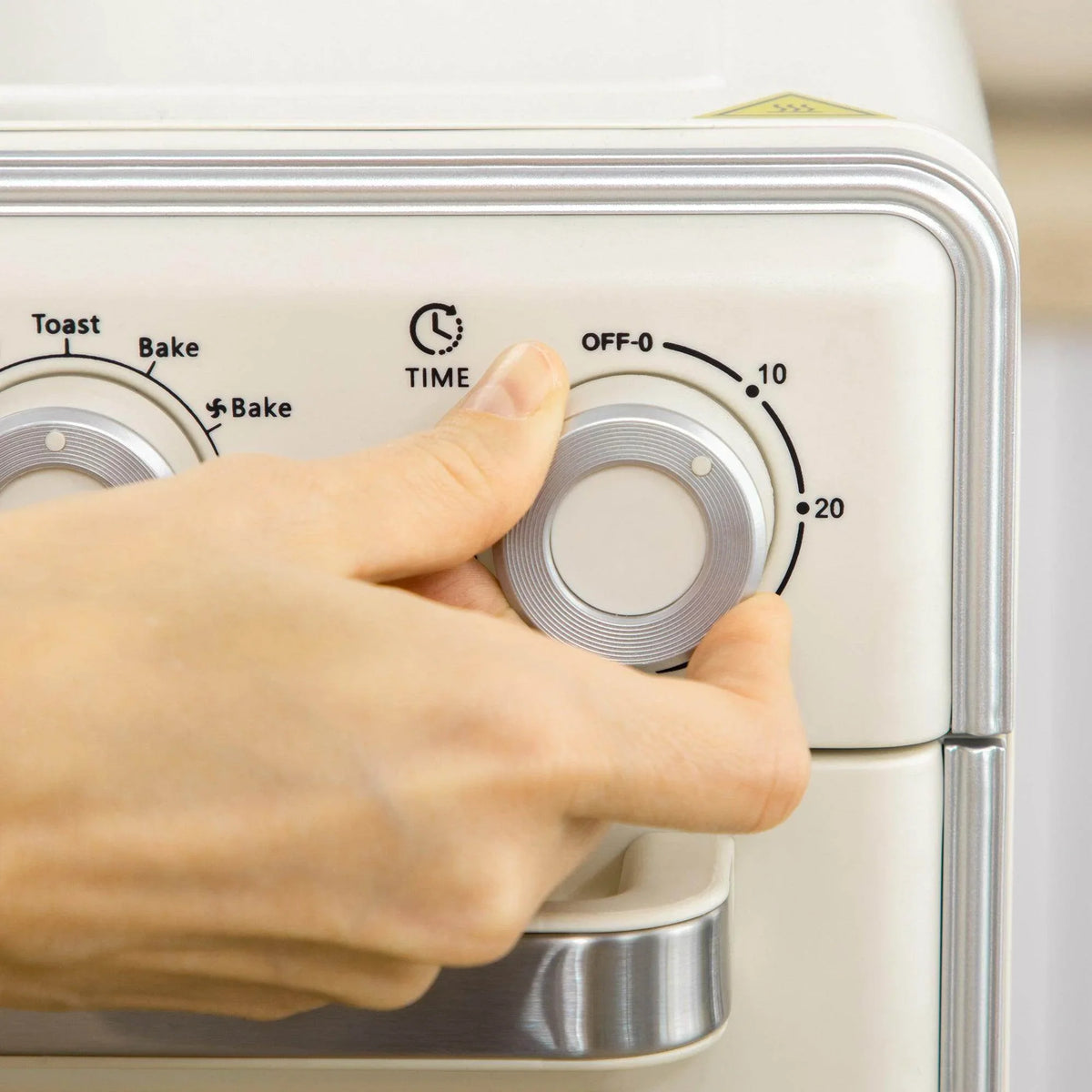 Hand turning the toaster oven timer knob on a cream front control panel