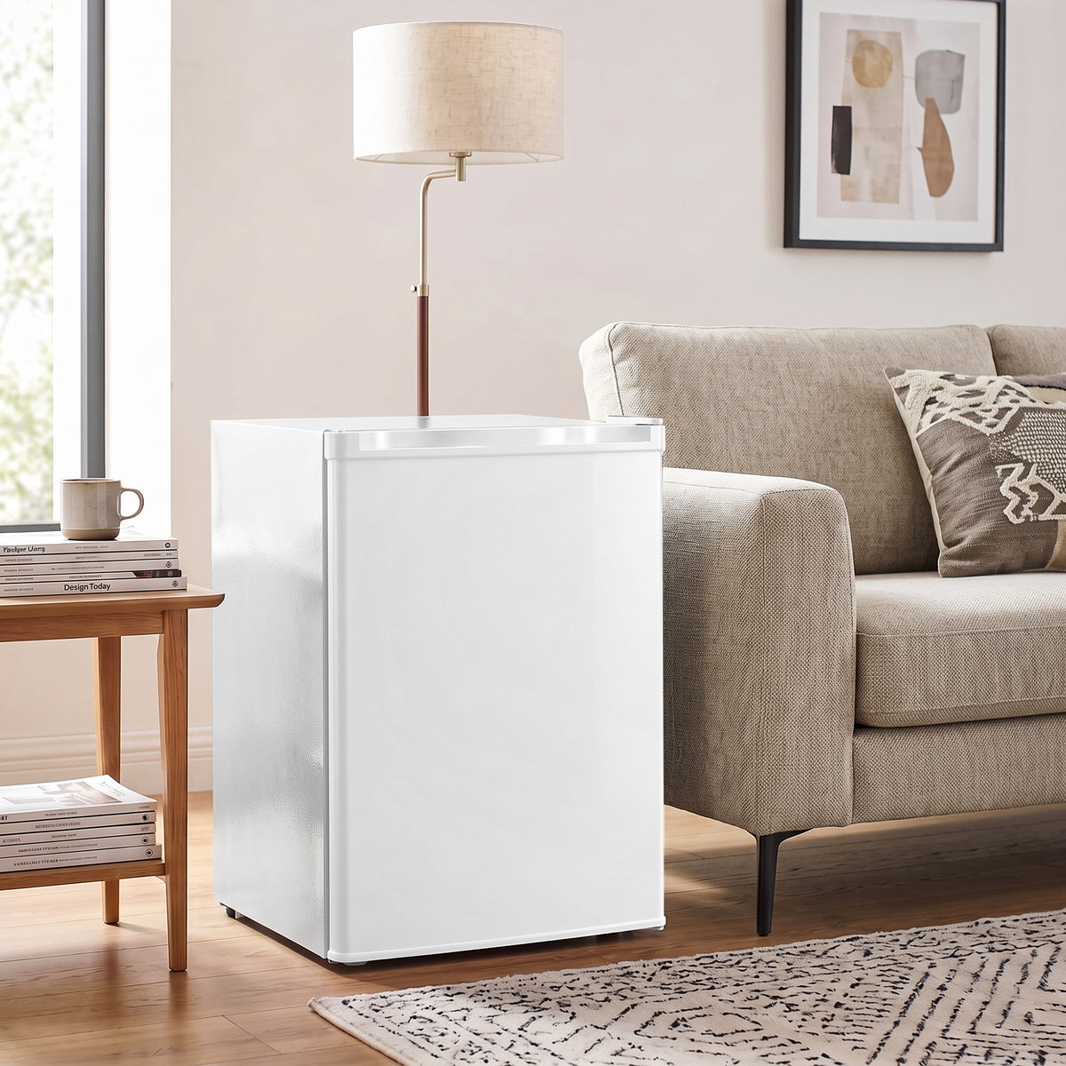 White mini fridge with chiller box standing next to a sofa, door closed.