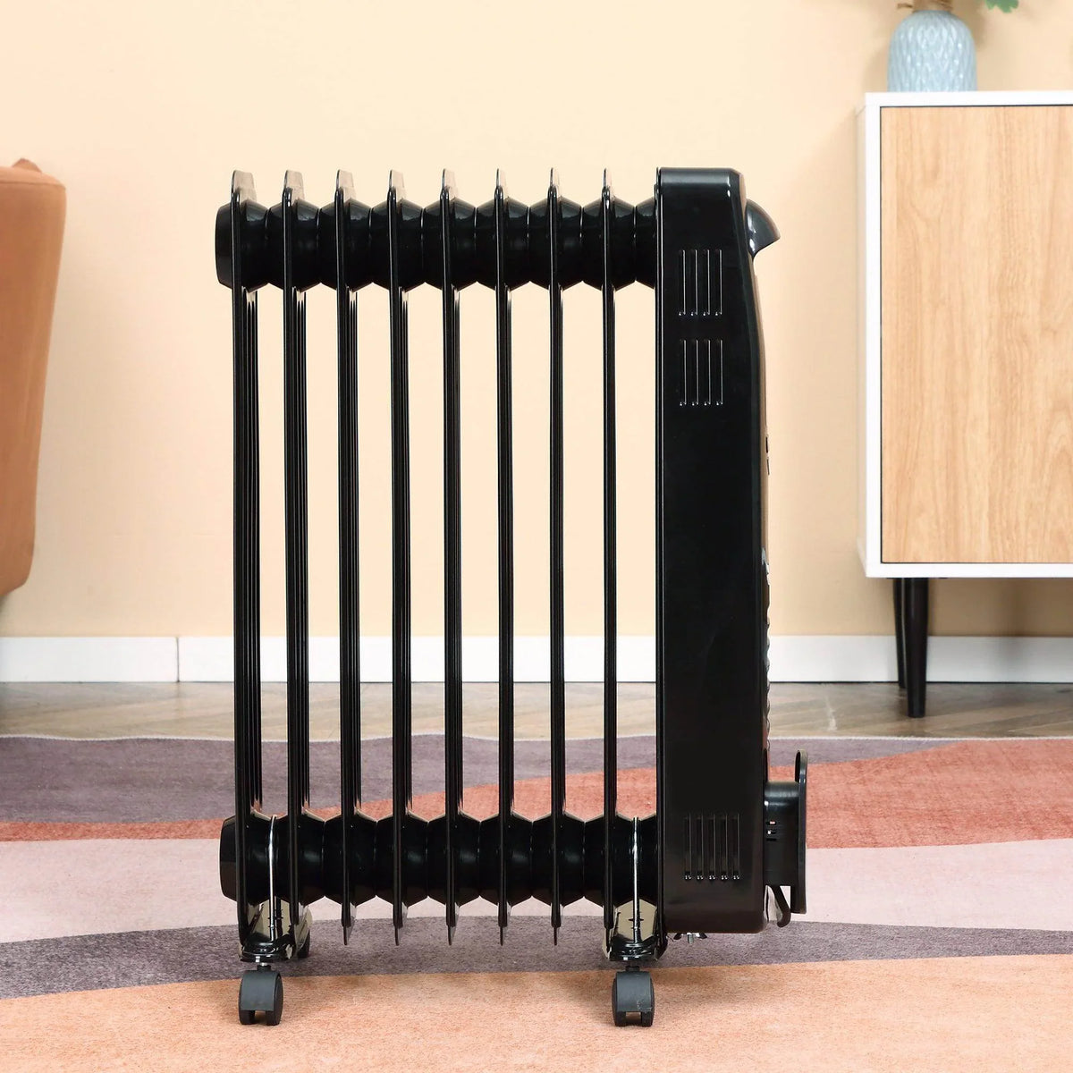 Black 9-fin oil filled heater with vertical fins and wheels, side view