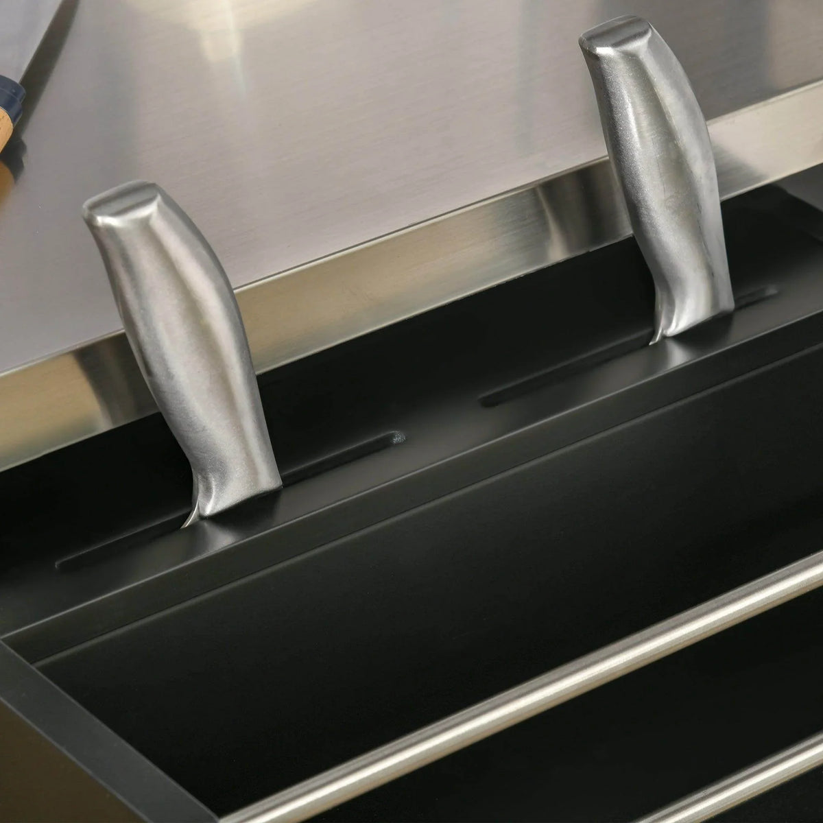 Stainless steel pull handles on black kitchen island drawer front with smooth metal edging.