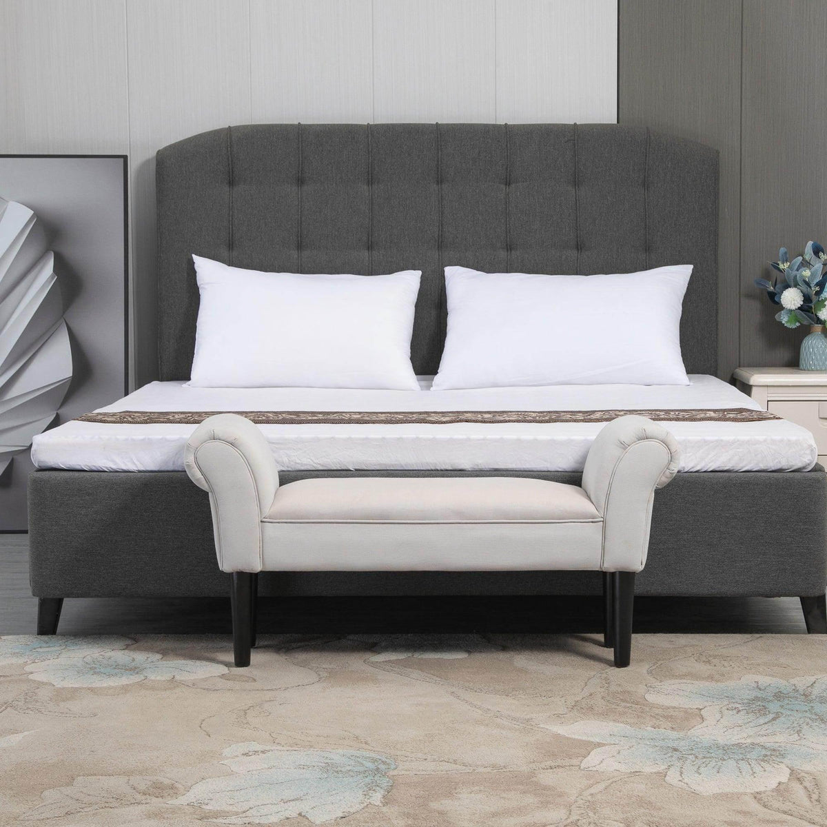 Grey ottoman bench with rolled arms and black legs, placed at bed foot