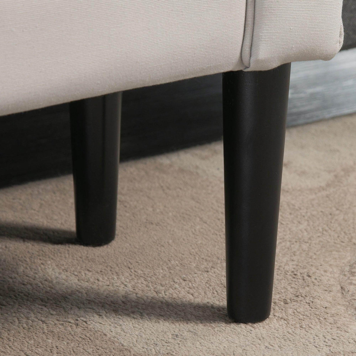 Black tapered legs under a light grey upholstered ottoman bench