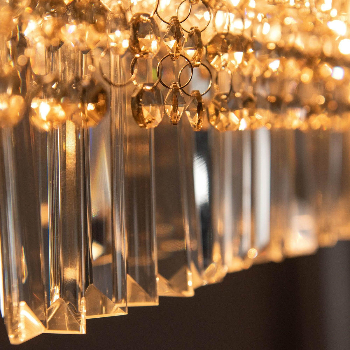 Close-up of gold crystal chandelier drops with dangling ring accents and warm light.