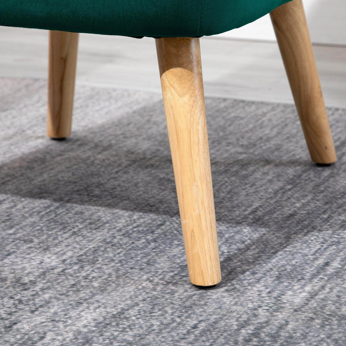 Light wood chair legs with protective foot pads under a green velvet seat