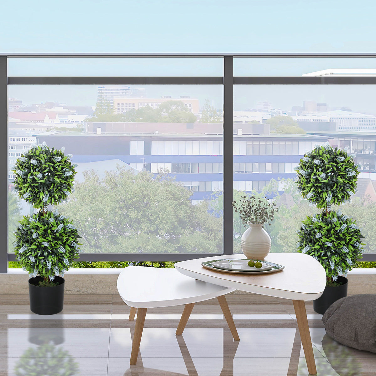 Two artificial green ball topiary trees in black pots near a white round table