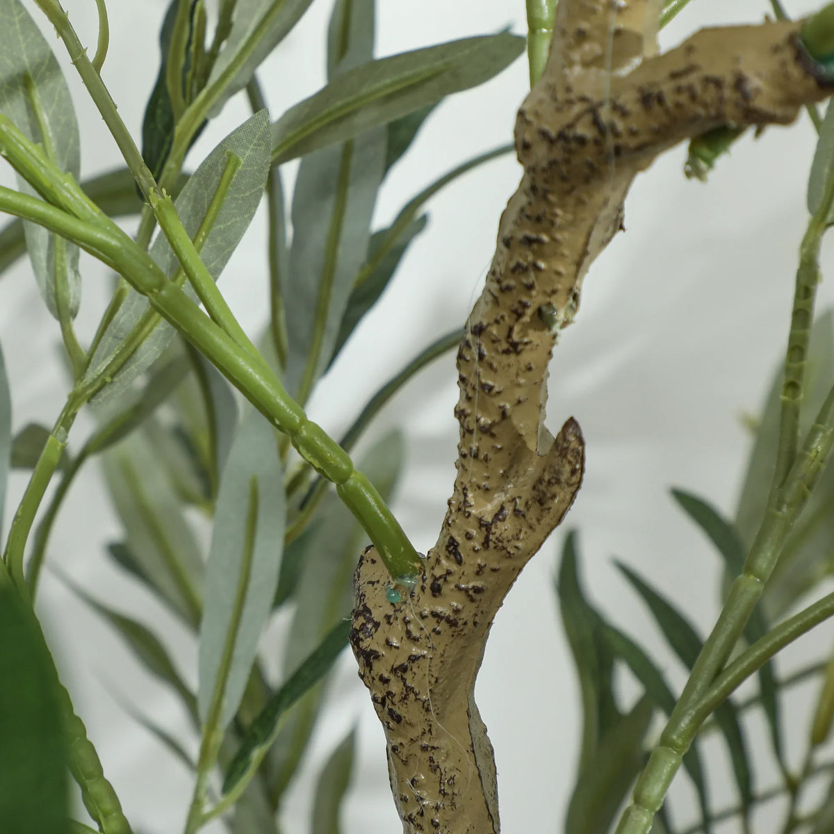 Close-up of artificial olive tree trunk texture and green leaf clusters in dark pot