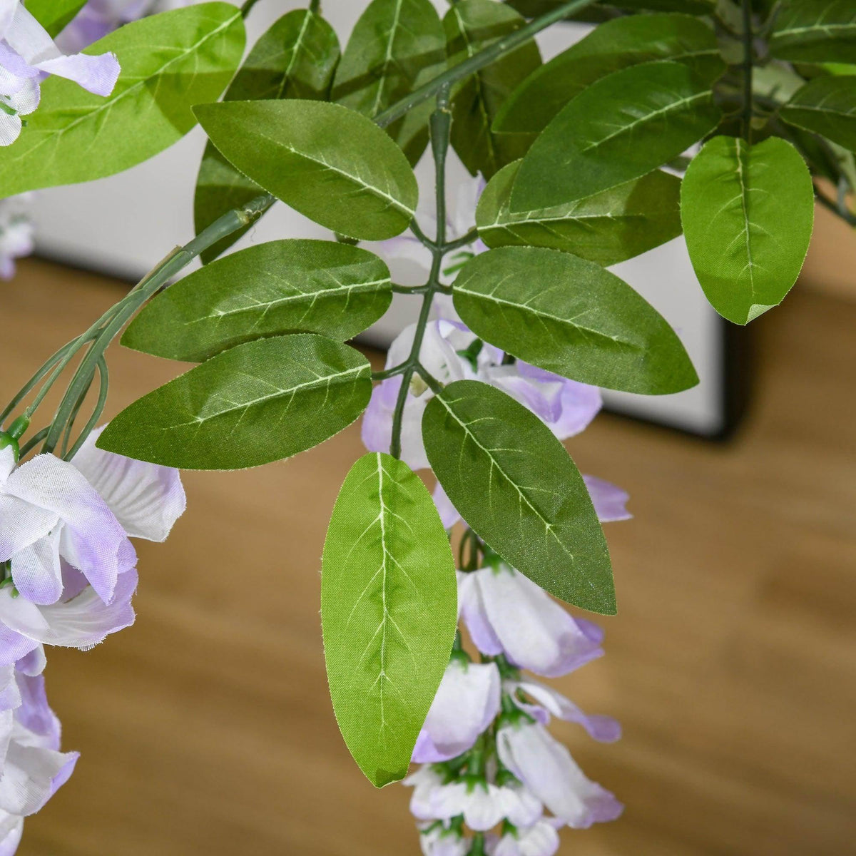 Close-up of artificial wisteria branches with green leaves and lilac and white blossoms