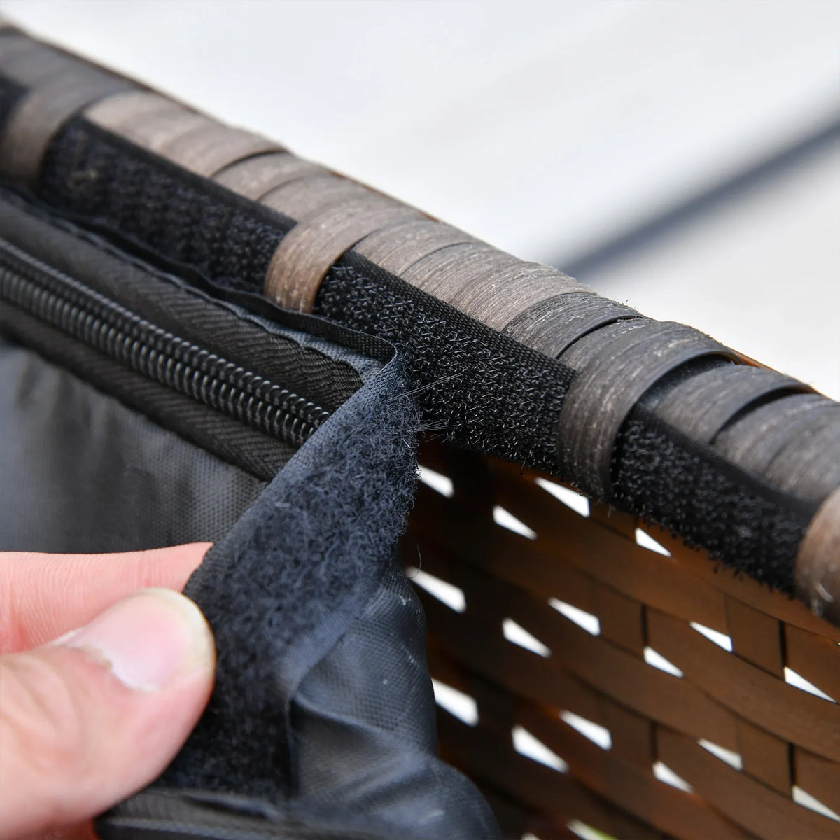 Close-up of hand adjusting dark cushion cover strap on woven rattan furniture