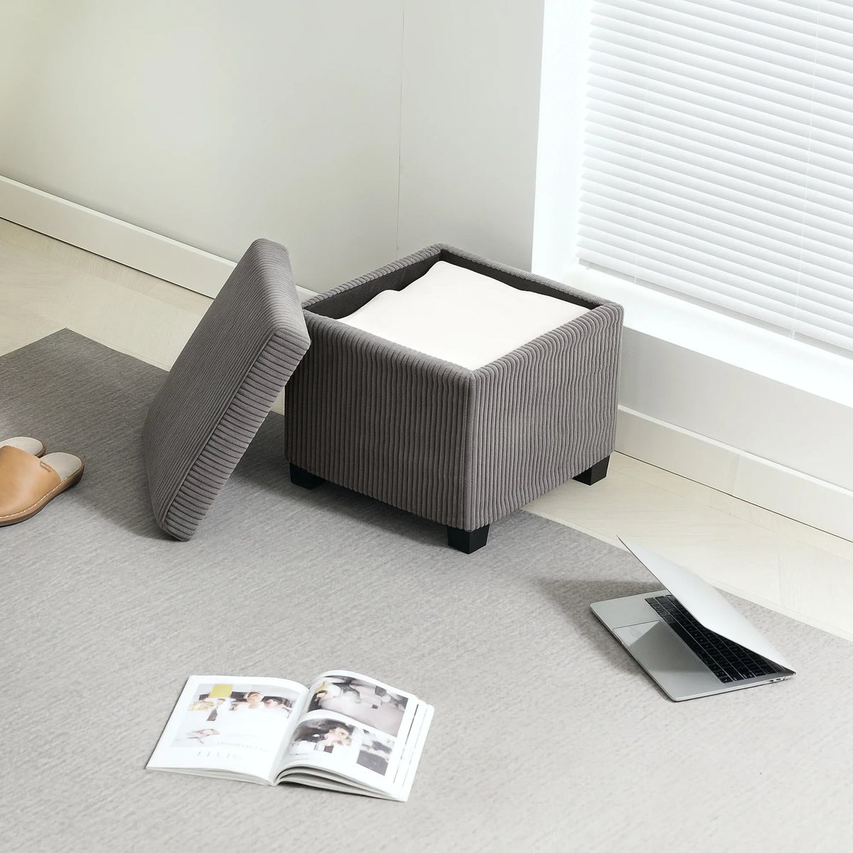 Grey corduroy storage ottoman bench with open lid and padded backrest against wall.