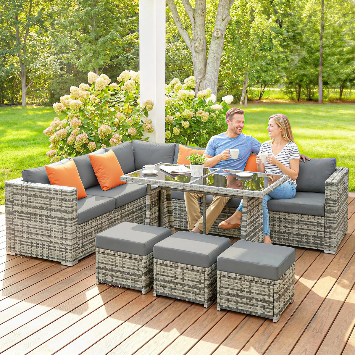 Gray woven outdoor rattan dining set with orange cushions, ottomans, and glass tabletop
