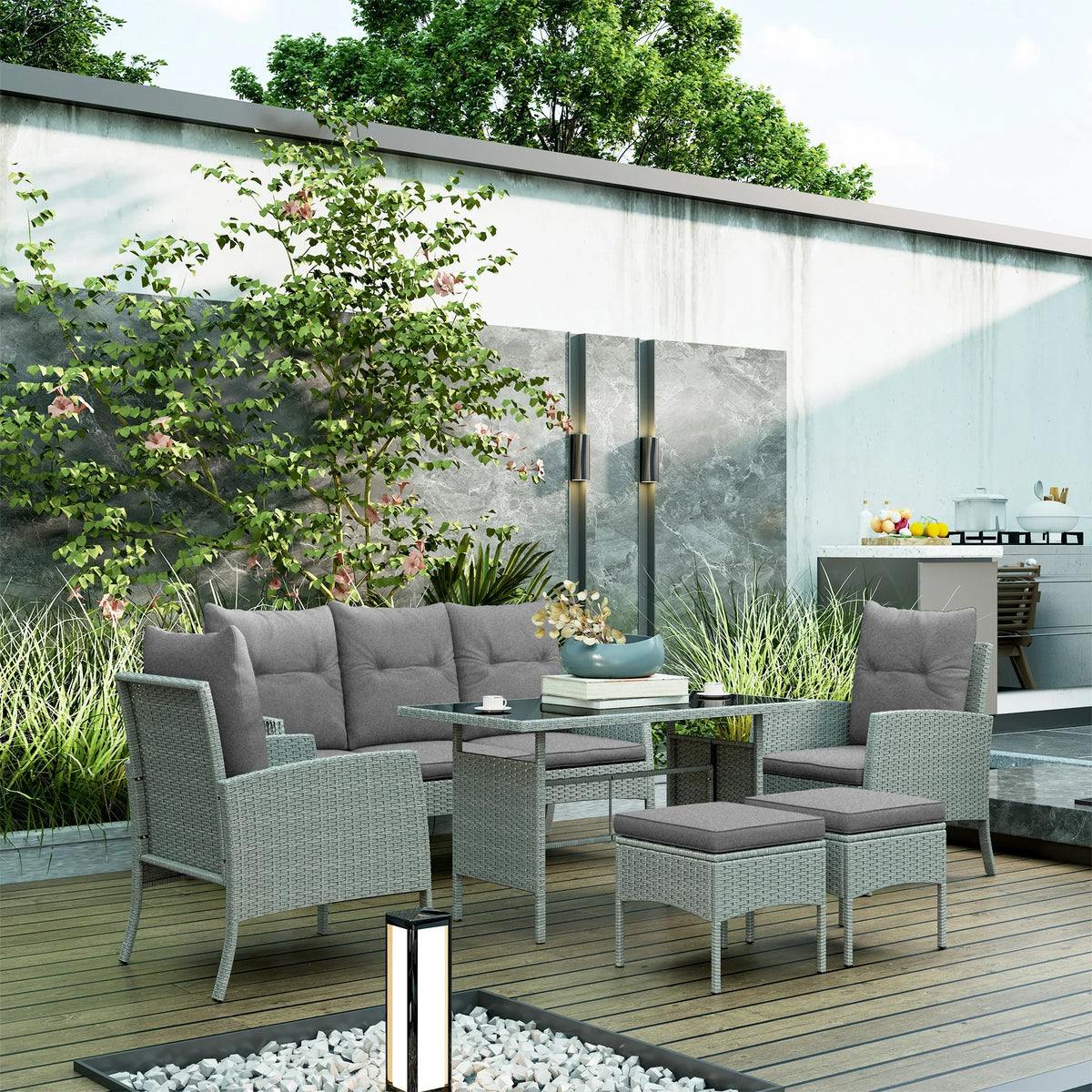 Grey rattan outdoor dining set with glass table, sofa, armchairs, and footstools