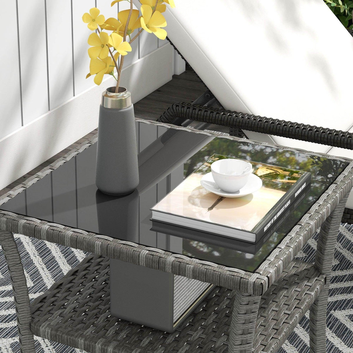 Grey rattan two-tier coffee table with clear glass top and visible open lower shelf