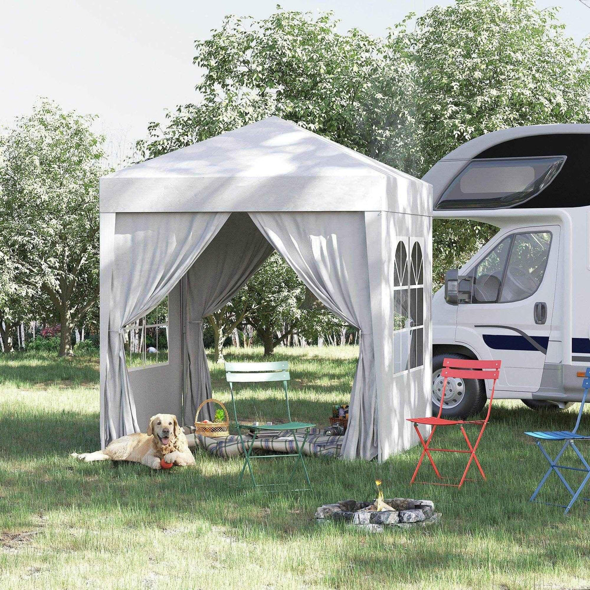 Gray pop-up gazebo with curtains, outdoor chairs, dog, and campfire beside RV in grassy yard