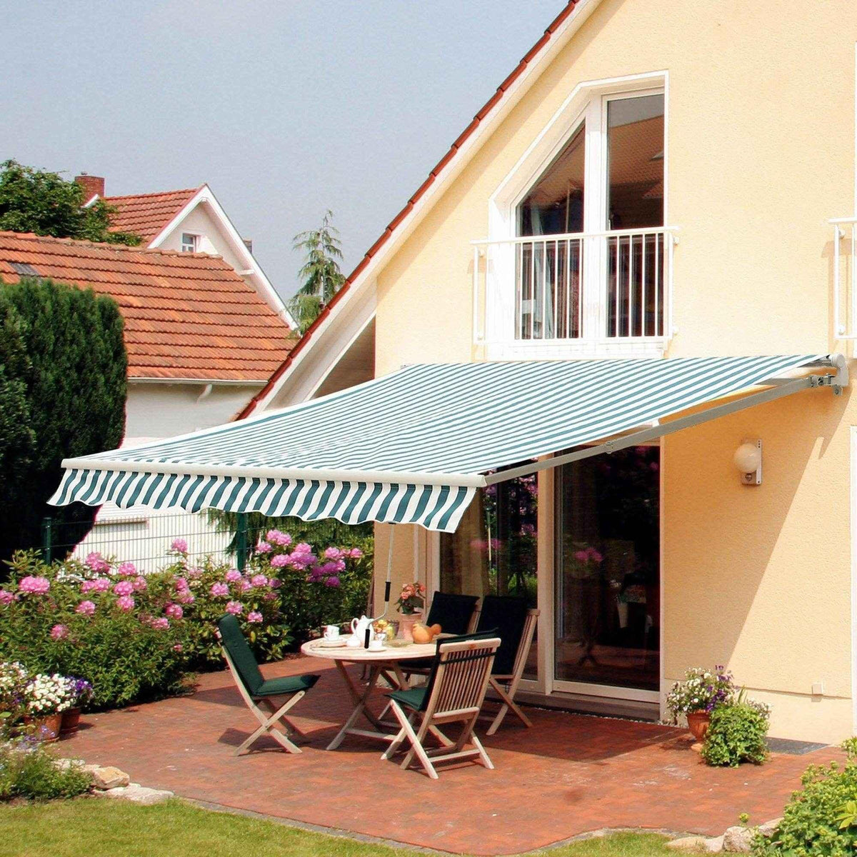 Green and white striped patio awning shading outdoor dining table and chairs on a brick terrace
