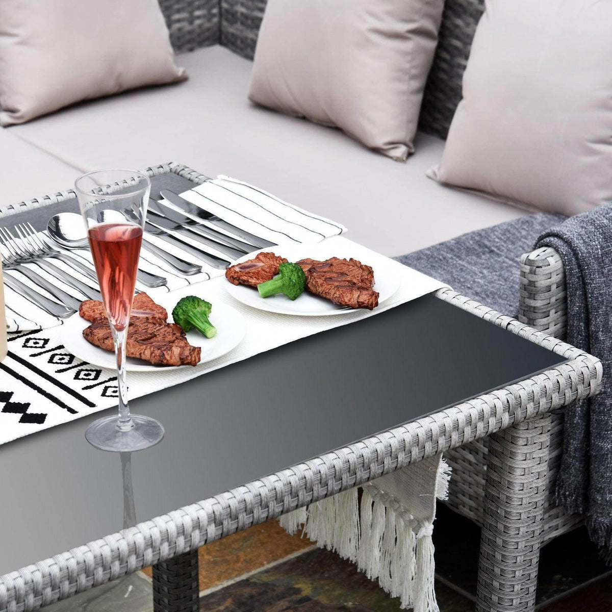 Corner dining set table with black top and white fringe trim on woven rattan frame
