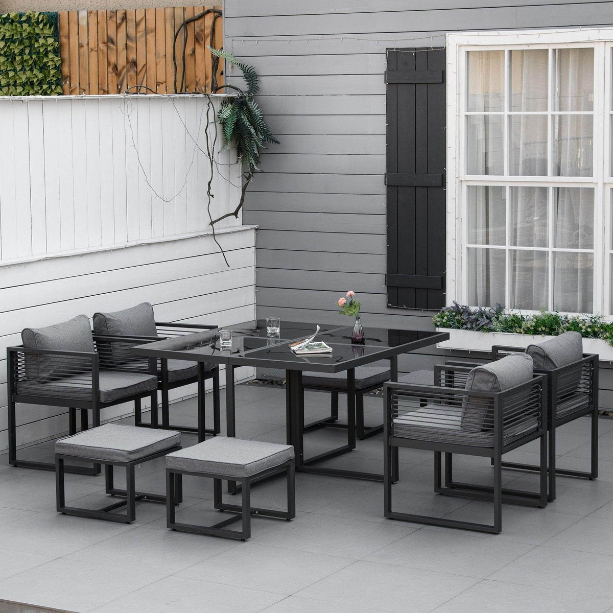 Outdoor dining set with black table, gray padded chairs, and two matching ottoman stools