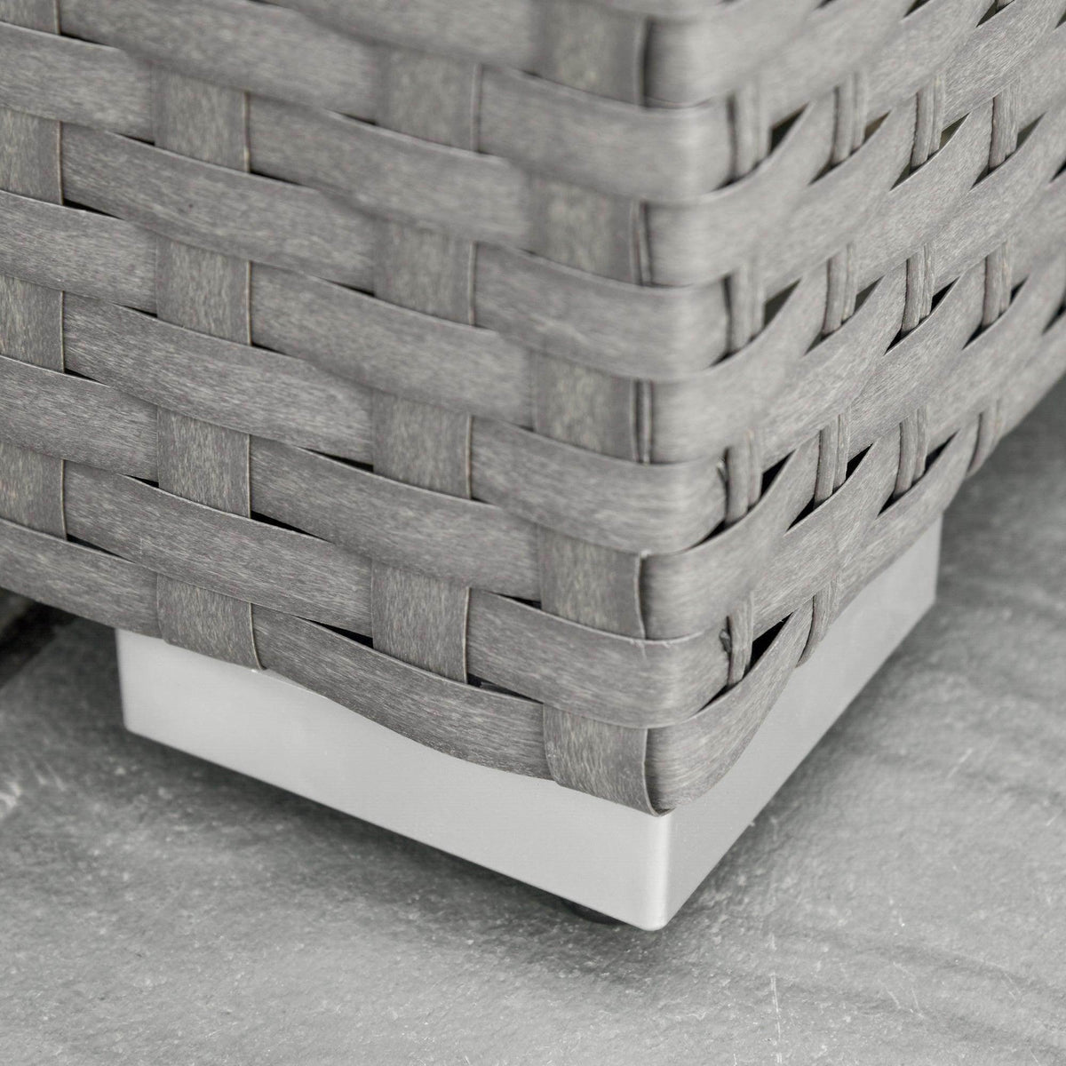 Grey woven rattan sofa frame corner with braided pattern and low white base pads.