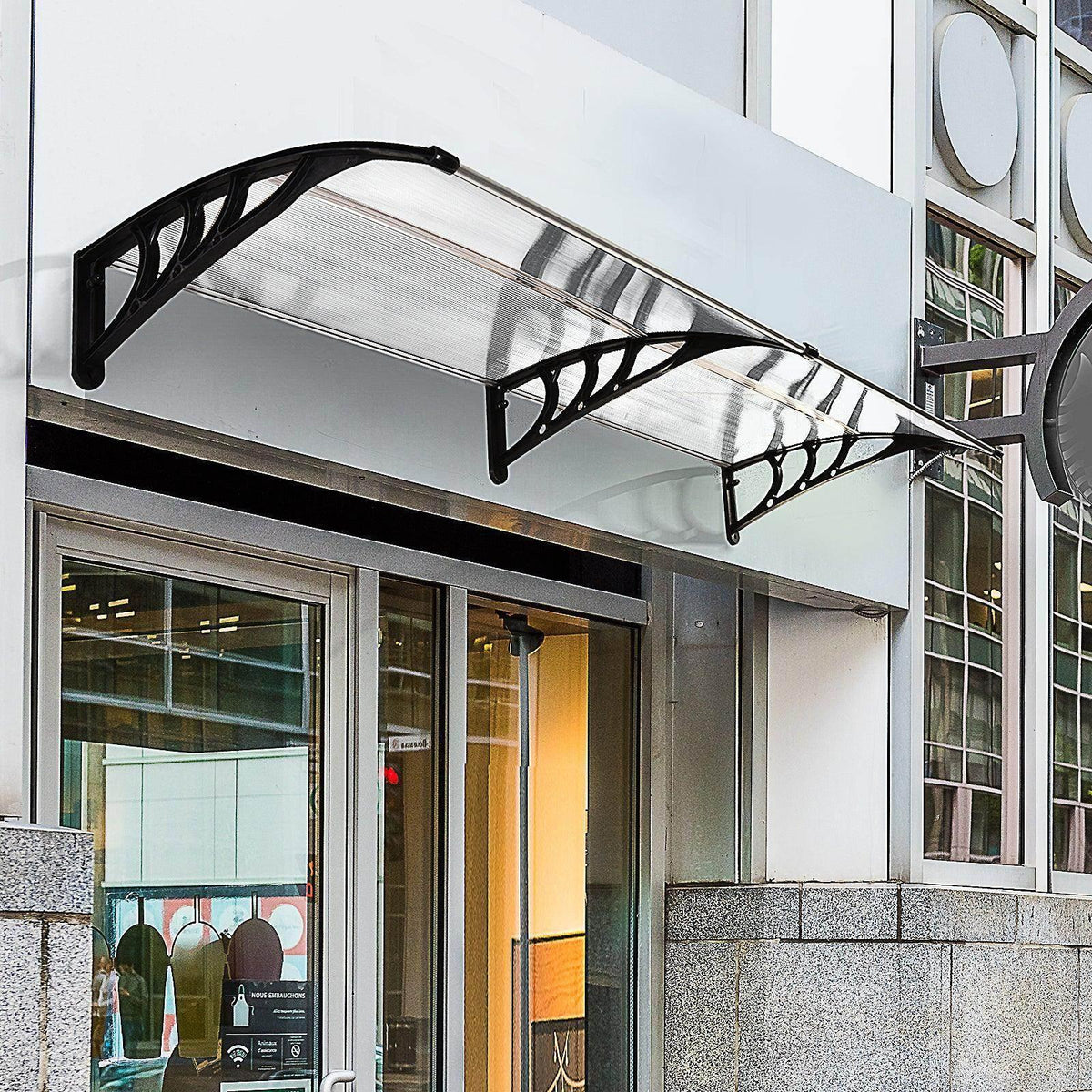 Clear window awning with black curved arms and transparent polycarbonate panel over a storefront