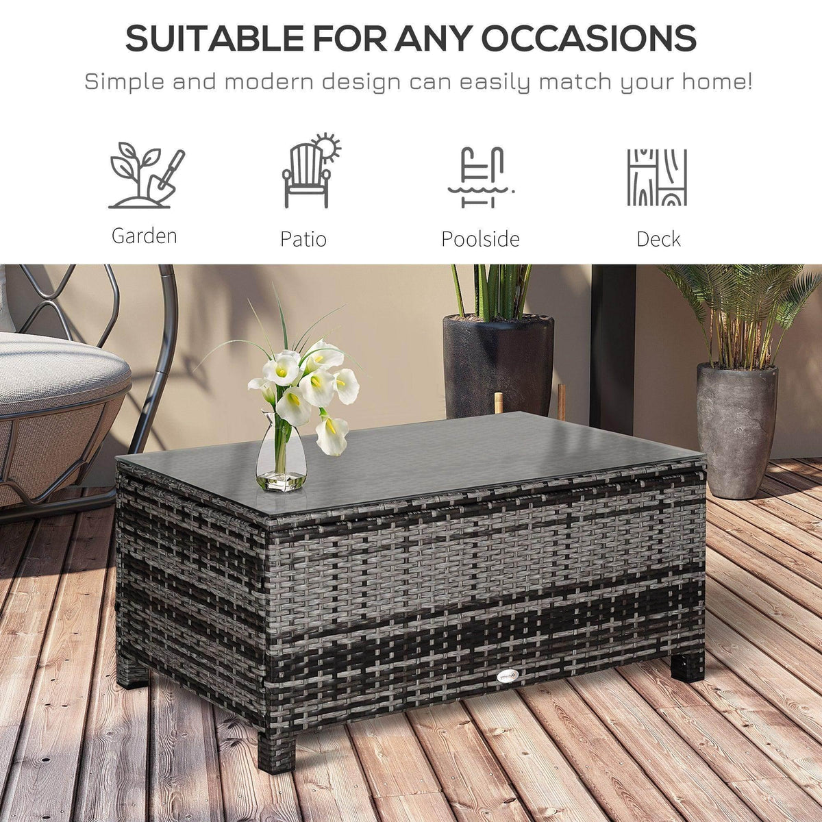 Grey rattan coffee table with clear glass top on outdoor deck with plants.