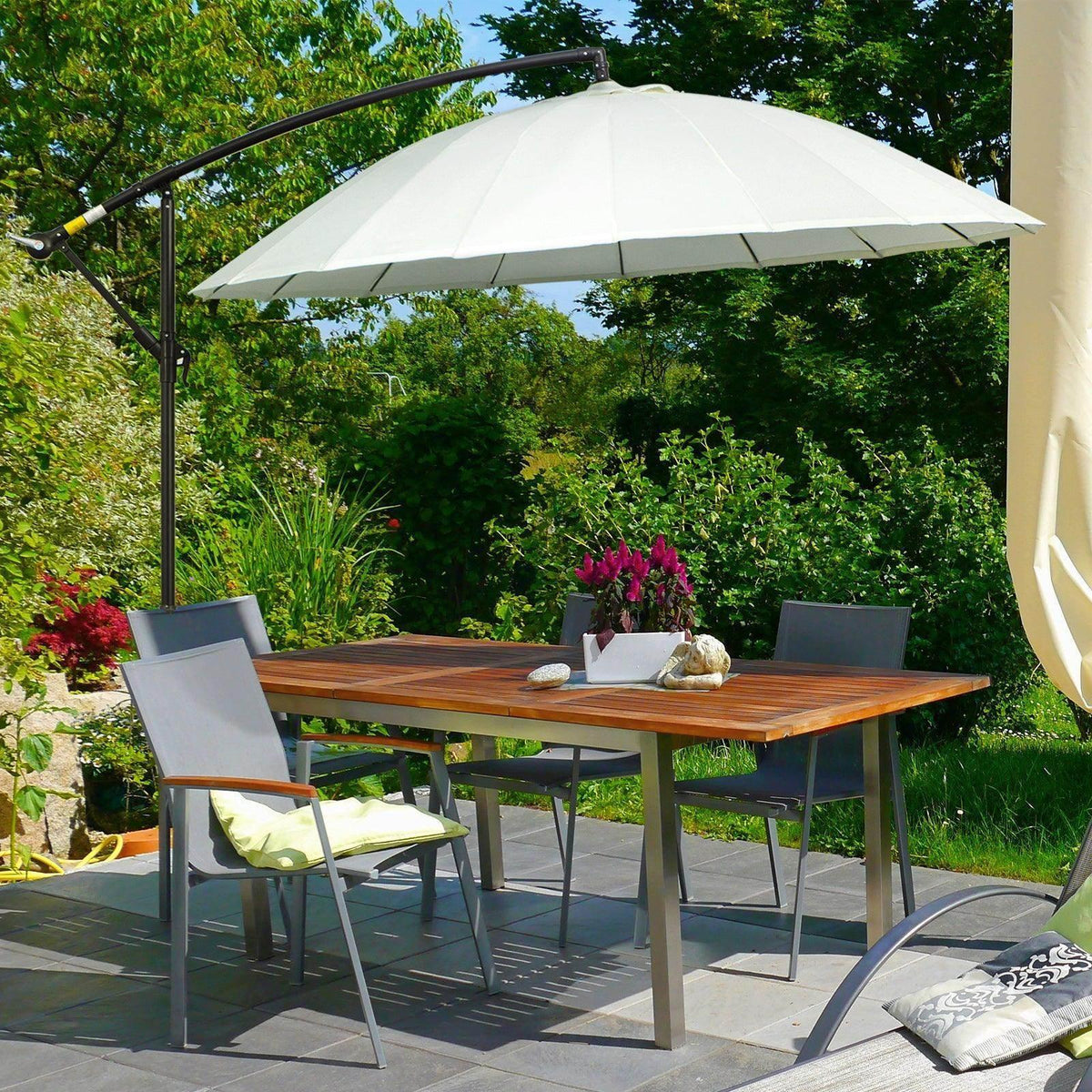 Off-white cantilever parasol over outdoor dining set with wooden table and chairs