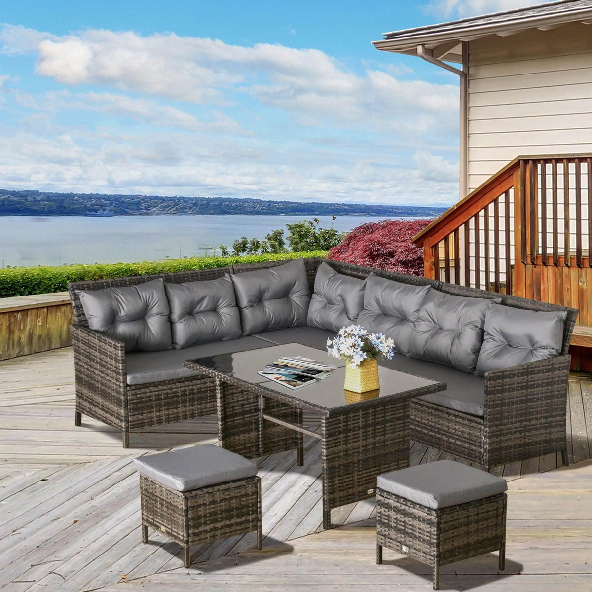 Grey rattan corner dining set with tufted seat cushions, glass table, and ottomans