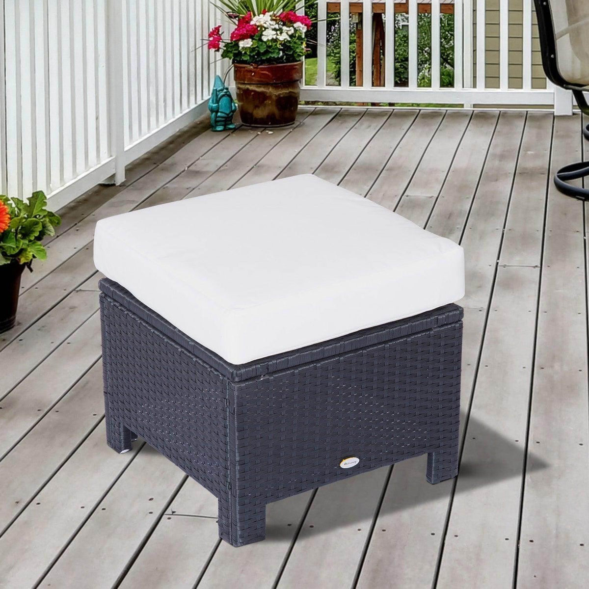 Black rattan ottoman with white cushioned top, outdoor corner view