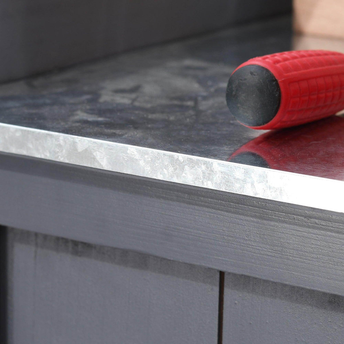 Galvanized metal tabletop edge on grey potting shed with a red tool on top