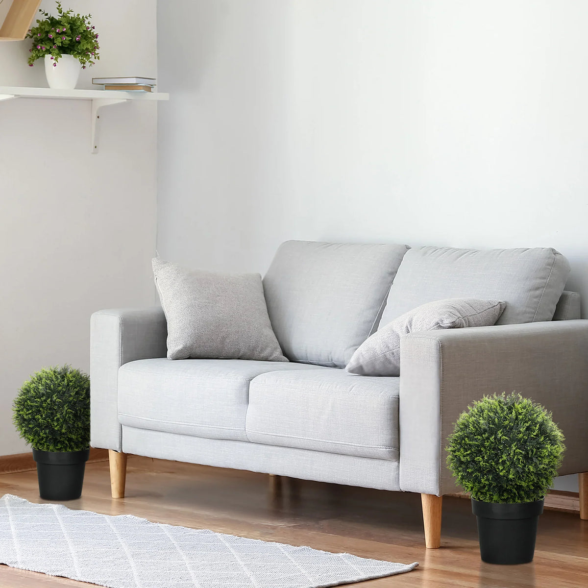 Green artificial topiary balls in black pots on floor beside a sofa