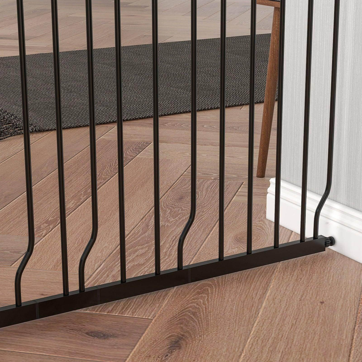 Black dog safety gate with vertical bars and base foot on wood floor