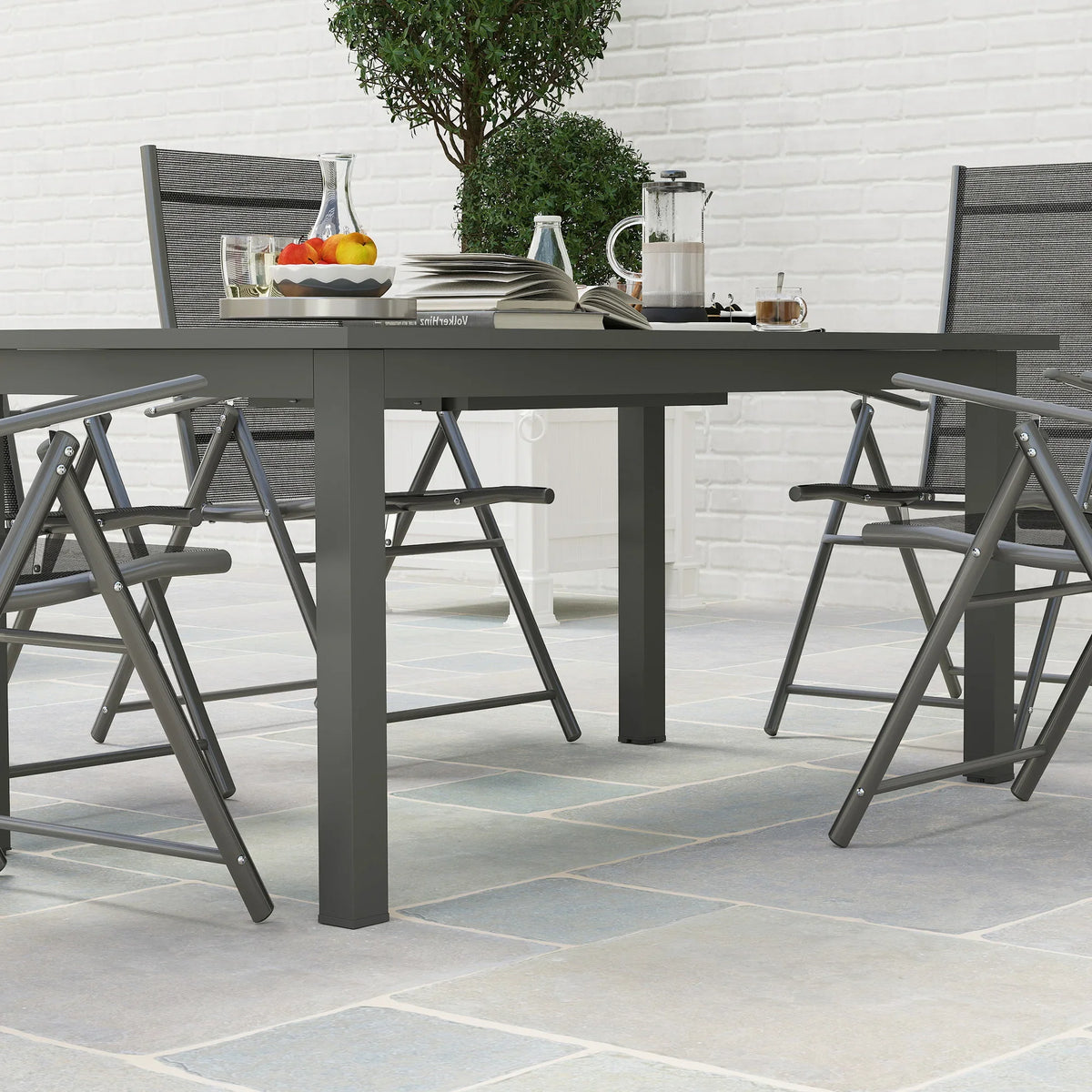 Grey outdoor dining table with slatted top and butterfly leaf, with black chairs