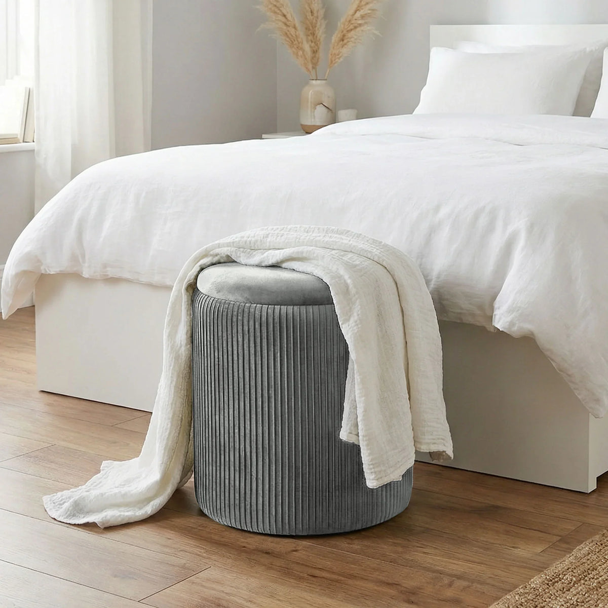 Grey ribbed round storage ottoman with cushioned top beside white bed